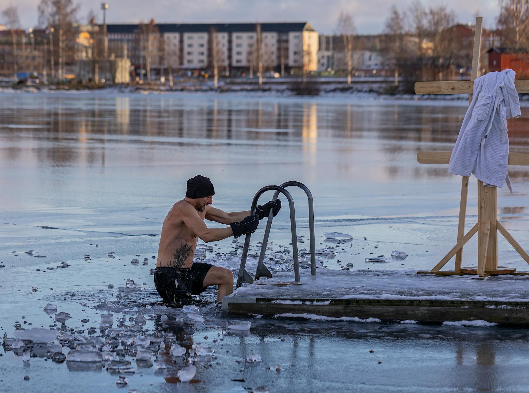 Hombre saliendo de un baño de hielo en lago helado al amanecer